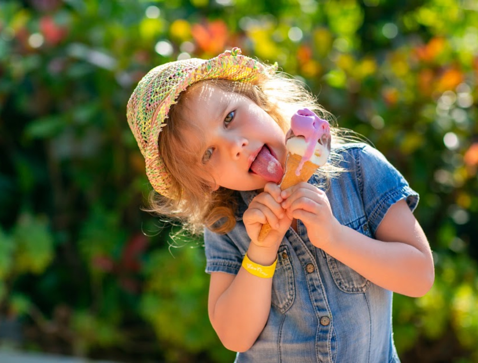 Curly haired little girl in a sun hat licking ice cream cone