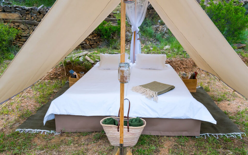 A glamorous tent with a bed and other amenities surrounded by nature shows what glamping can be like.  